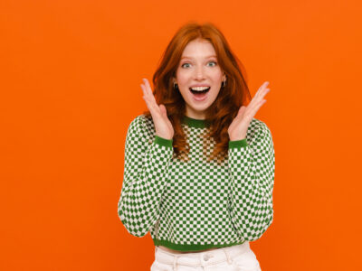 Excited ginger woman in plaid sweater expressing surprise at camera